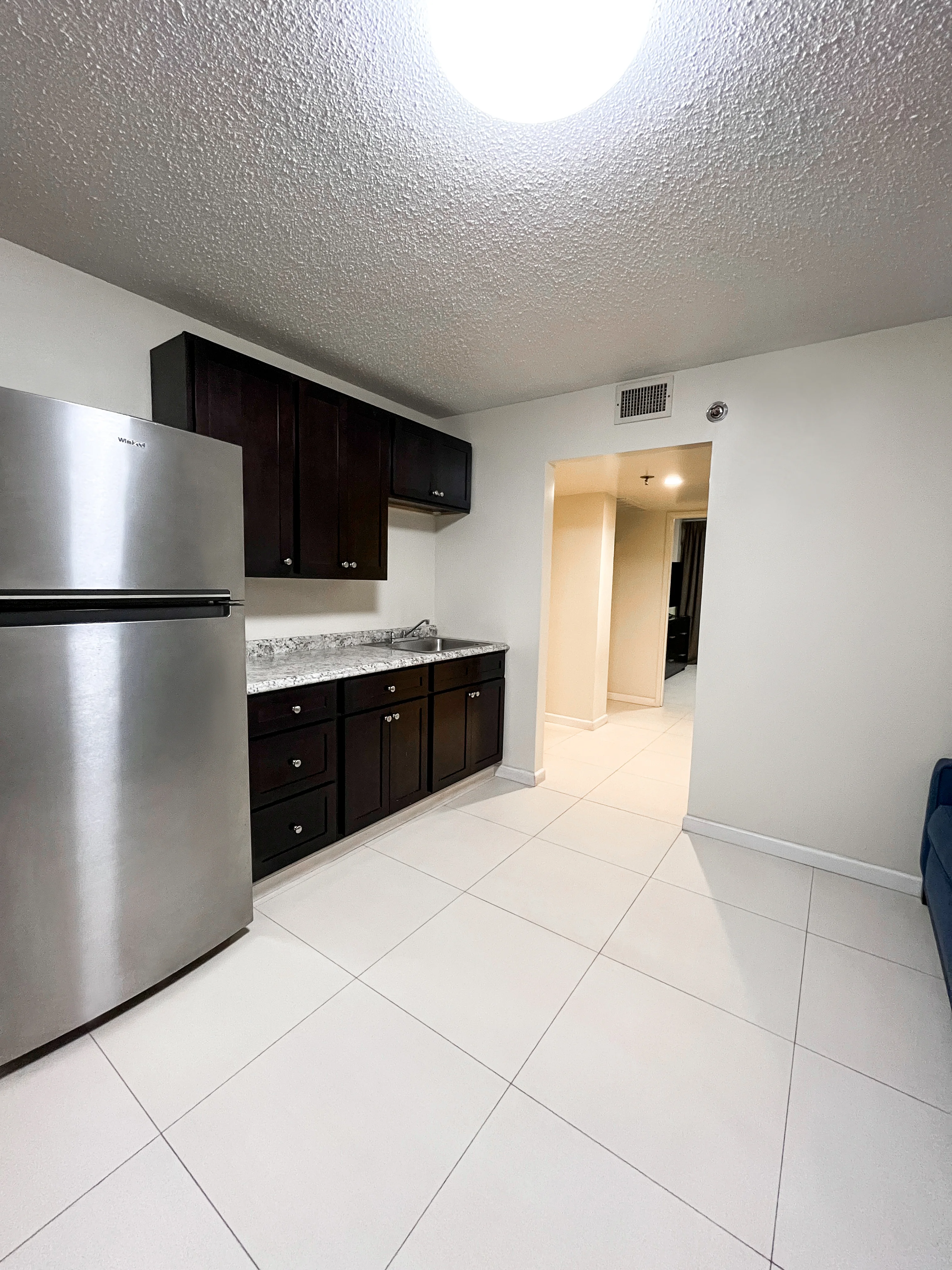 Apartment kitchenette with dark cabinets and stainless-steel refrigerator
